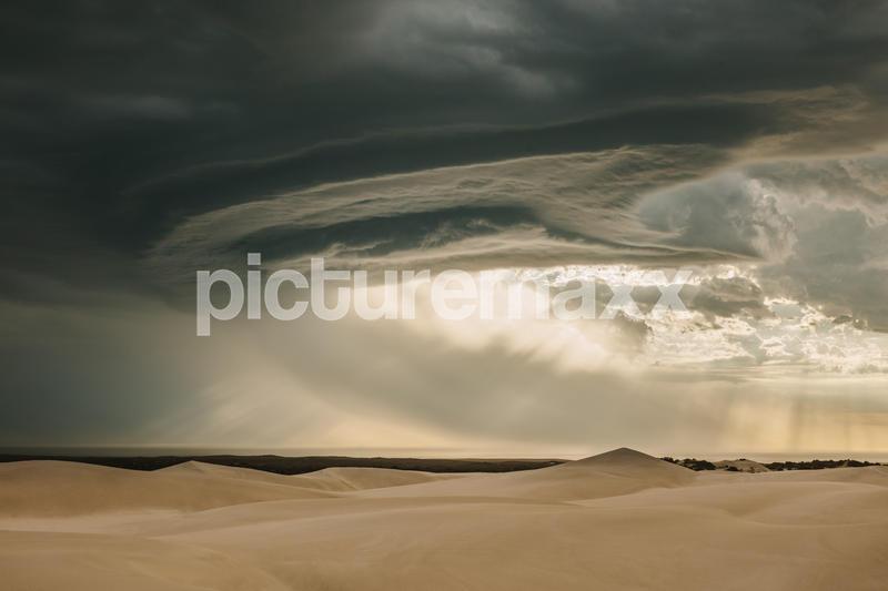 View of dramatic sky and sand dunes in desert. Dark clouds over sand dunes during evening. Moody sky.