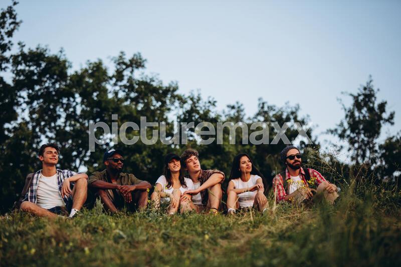 Meet sunset, new day. Six multiethnic friends, young men and women walking, strolling together in summer forest, meadow, outdoors. Lifestyle, friendship, having fun, weekend and resting concept.