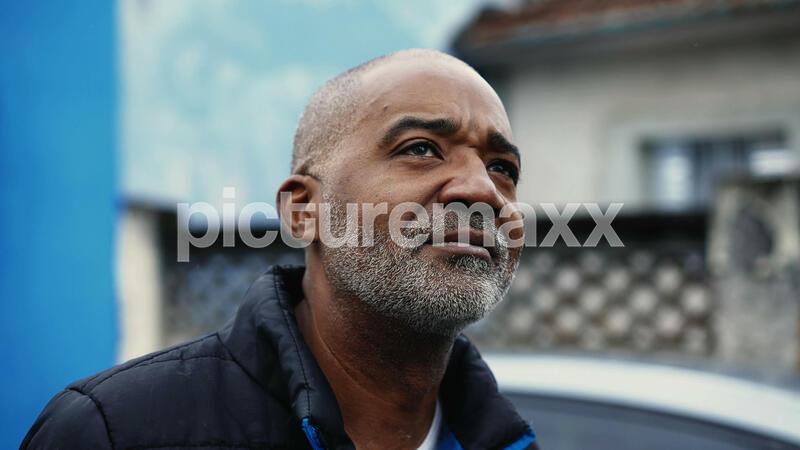 Pensive African American mature man in 50s observing urban surroundings while strolling in street, close-up face tracking shot of a black middle aged person with thoughtful gaze