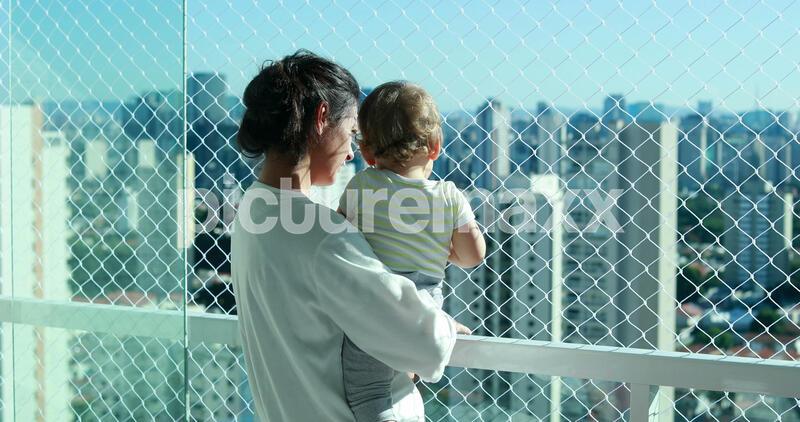 Mom holding baby looking at city view from apartment balcony with safety net