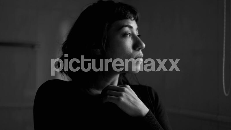 A contemplative young hispanic woman standing by window thinking. A pensive latin girl in monochromatic